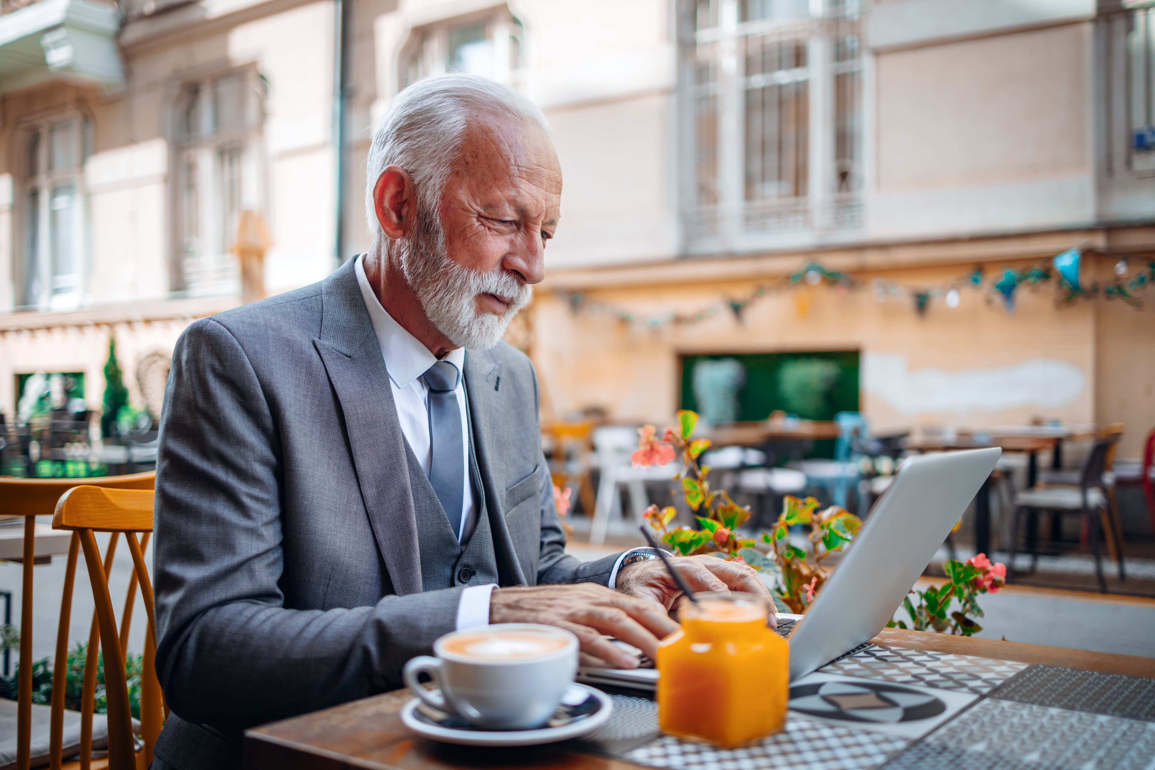 A person wearing a suit looks at a computer while seated at an outdoor table.
