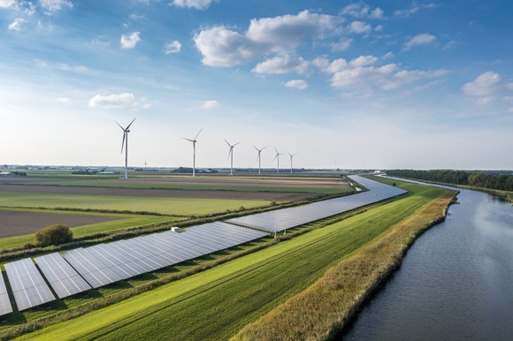 Windmills and solar panels alongside a river.
