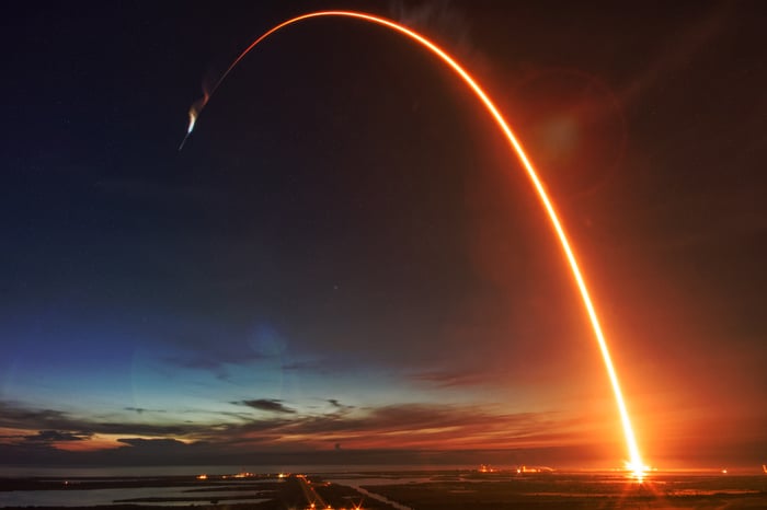A rocket's path glows in orange at sunset.