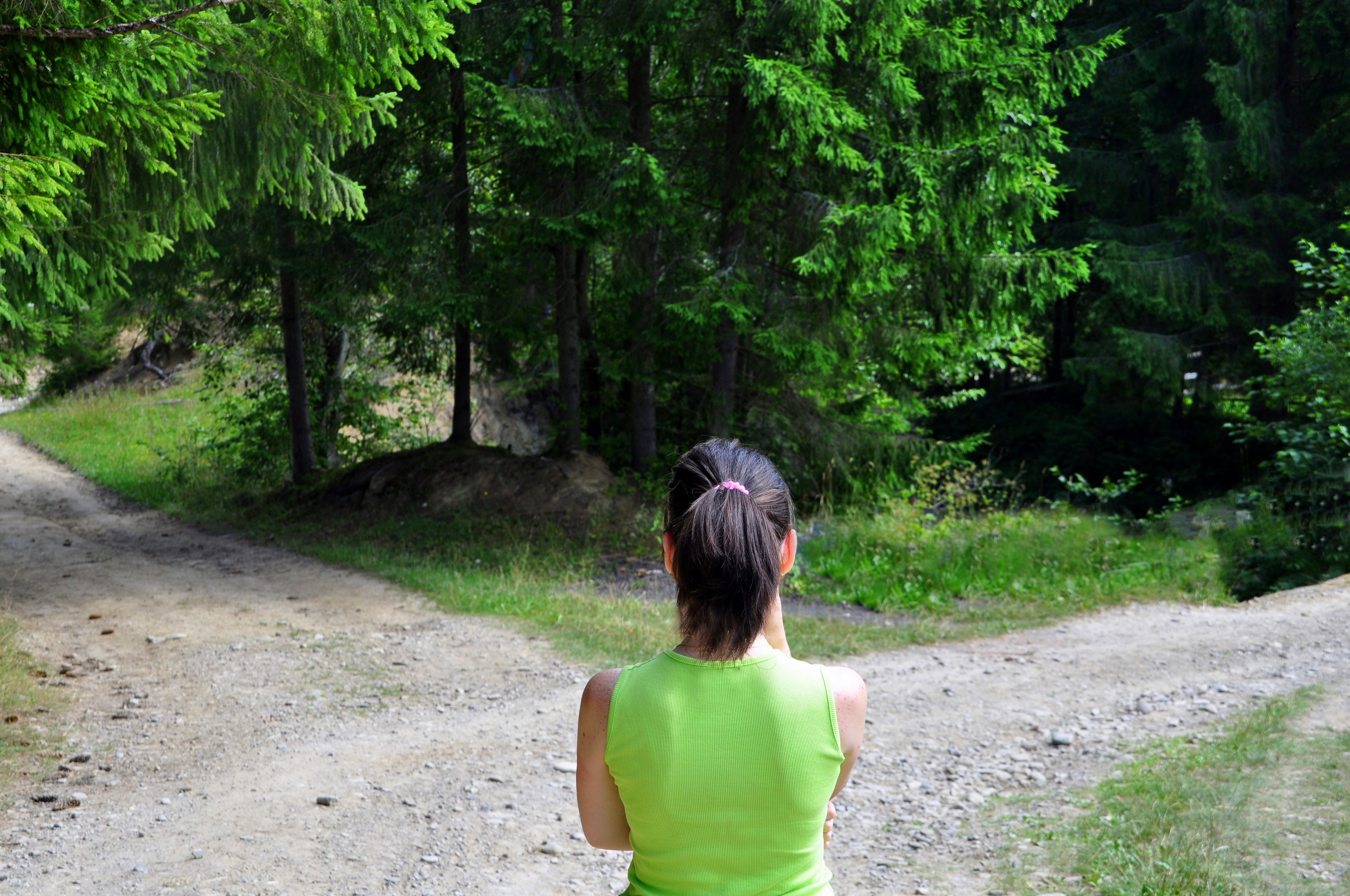 A person on a forest trail looking at a fork in the road. 