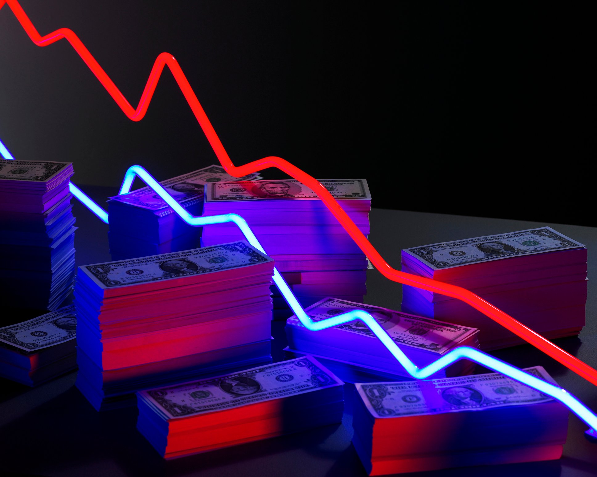 Red and blue neon lights pointing downward on top of a large cash pile.