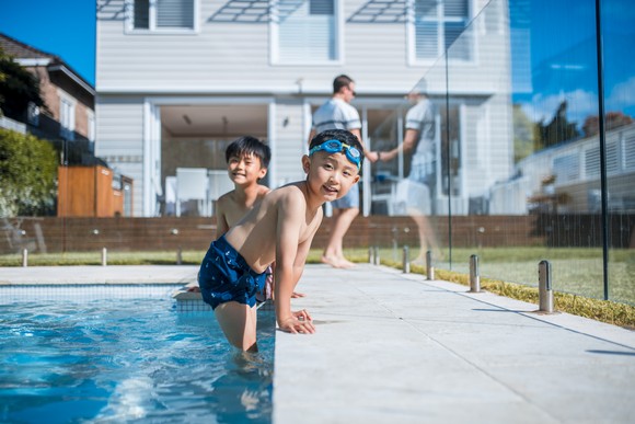 Two children in a suburban swimming pool with an adult standing in the background.