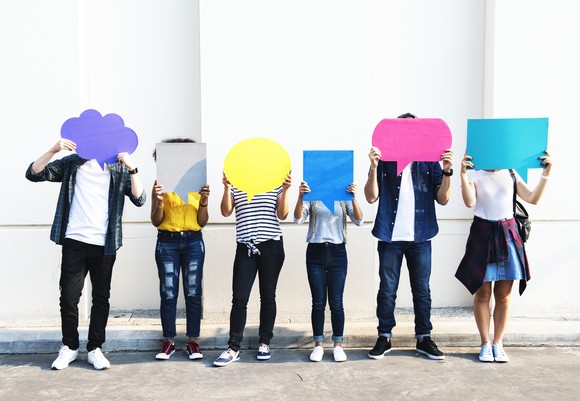 Six young people hold cardboard cutouts of speech and thought bubbles.
