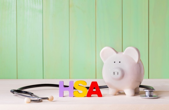 Piggy bank with colorful “HSA” letters and a stethoscope on a desk.