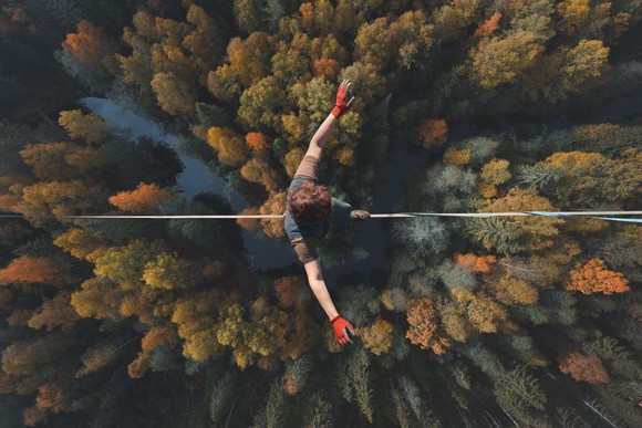 A person walks on a tightrope high above the ground.