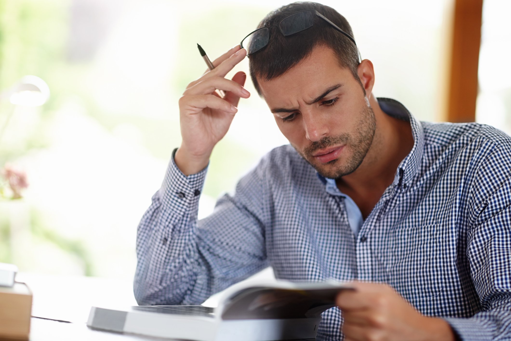 An investor looks at a book in consternation while sitting at a table.