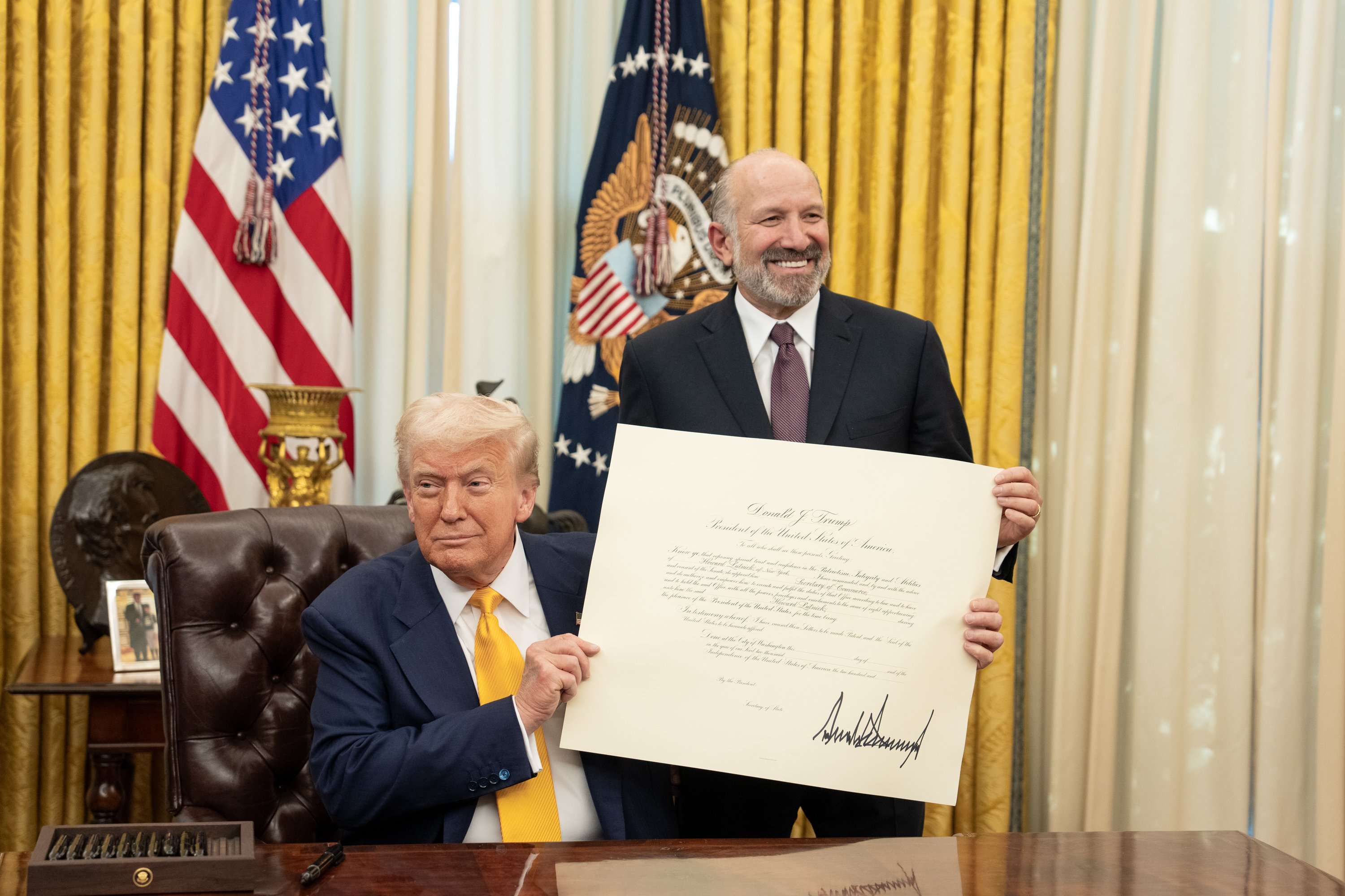 President Donald Trump holds a signed document with Commerce Secretary Howard Lutnick.