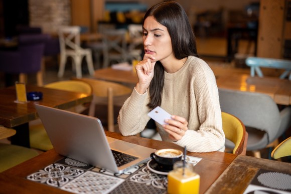 A person looks at a laptop and holds a credit card.