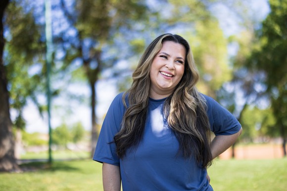 Person wearing a blue shirt, standing outside and smiling. 