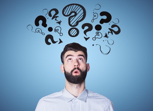 Young man looking up at a series of question marks. 