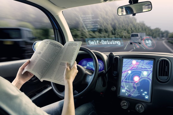 A driver reads a book in a self-driving car.