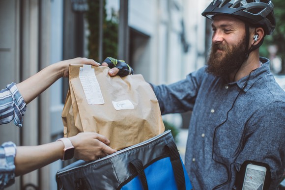 A food delivery person hands a food order to another person. 