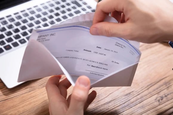 An envelope is opened over a desk, revealing a check inside.