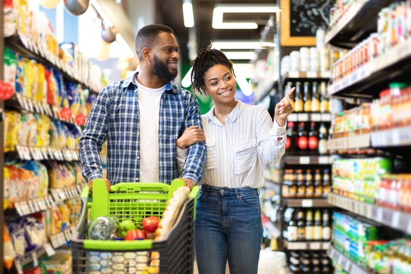 A smiling young couple checking out goods on the shelves of a grocery store. 