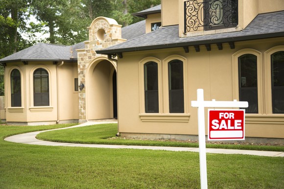 The front of a large, single-family home, with a "For Sale" sign in the front yard.