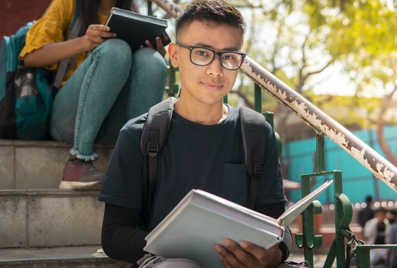 Person sitting outside, reading textbook.