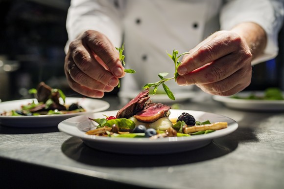 A chef preparing a plate of steak with veggies. 
