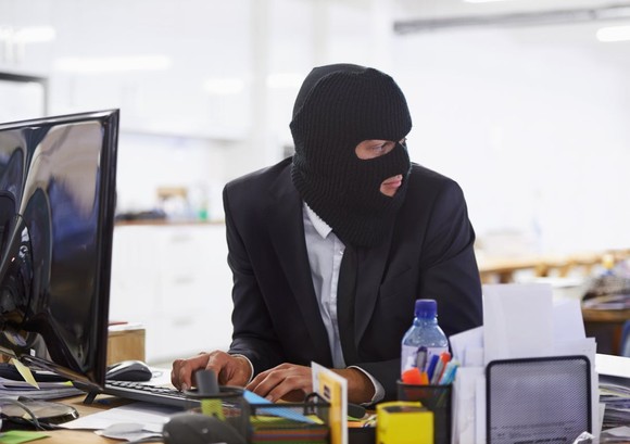 Person in a balaclava, typing on a computer keyboard. 
