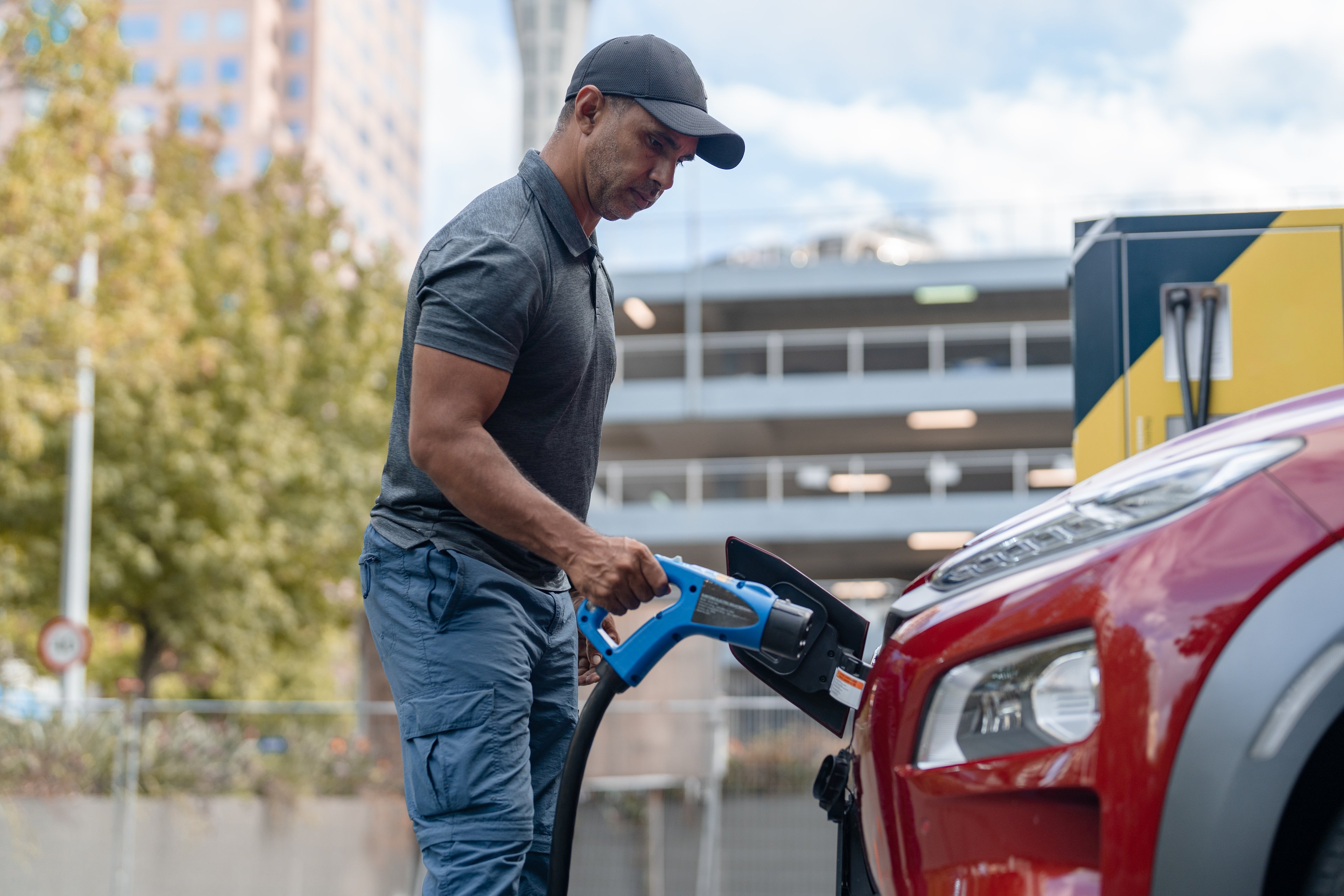 A person plugs an electric vehicle (EV) into an outdoor charging station.
