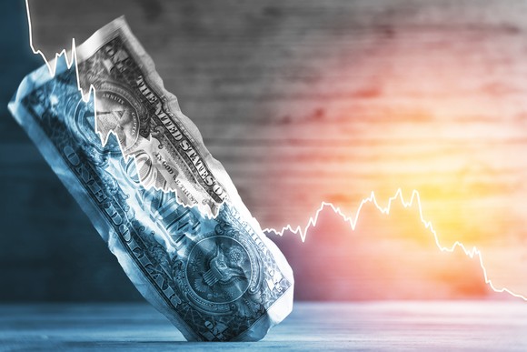 A downward graph line superimposed over a wrinkled dollar bill.