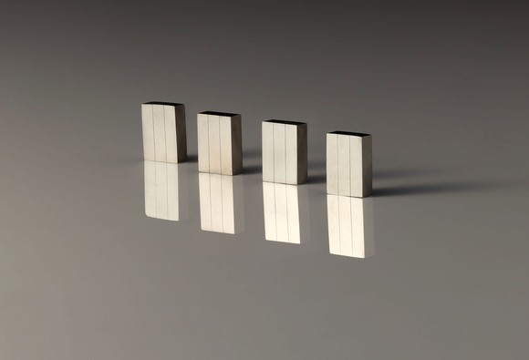 Four NdFeB magnets standing upright on a reflective surface. 