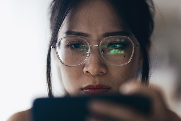 A person looking at their phone, with the reflection of a stock chart in their glasses