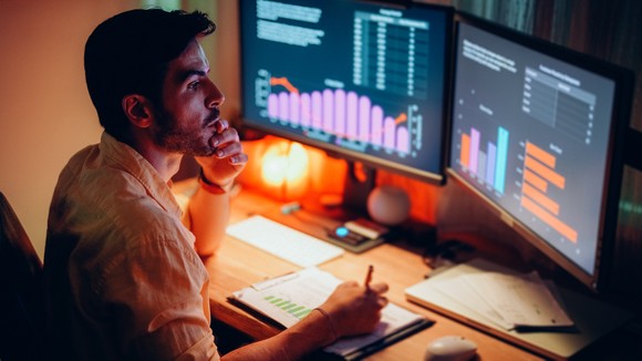 Man takes notes as he looks at computer screen showing investments.