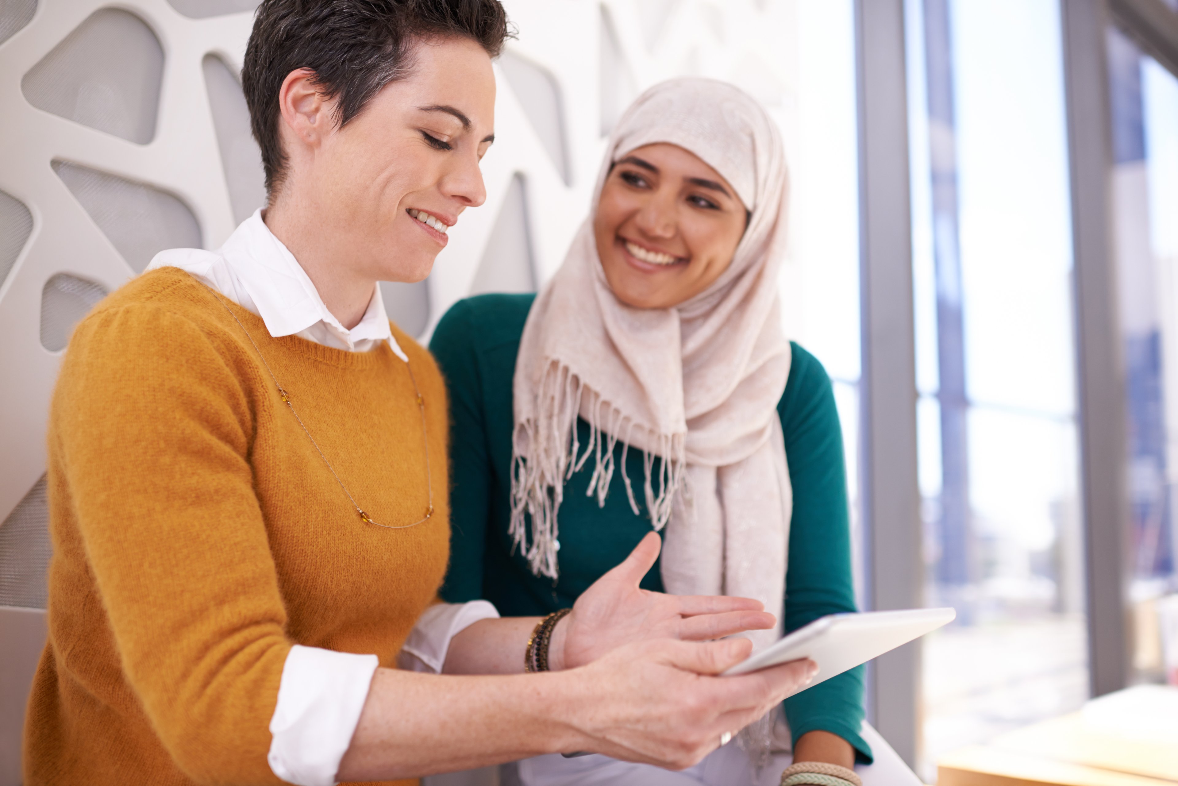 person in hijab talks to other person with tablet