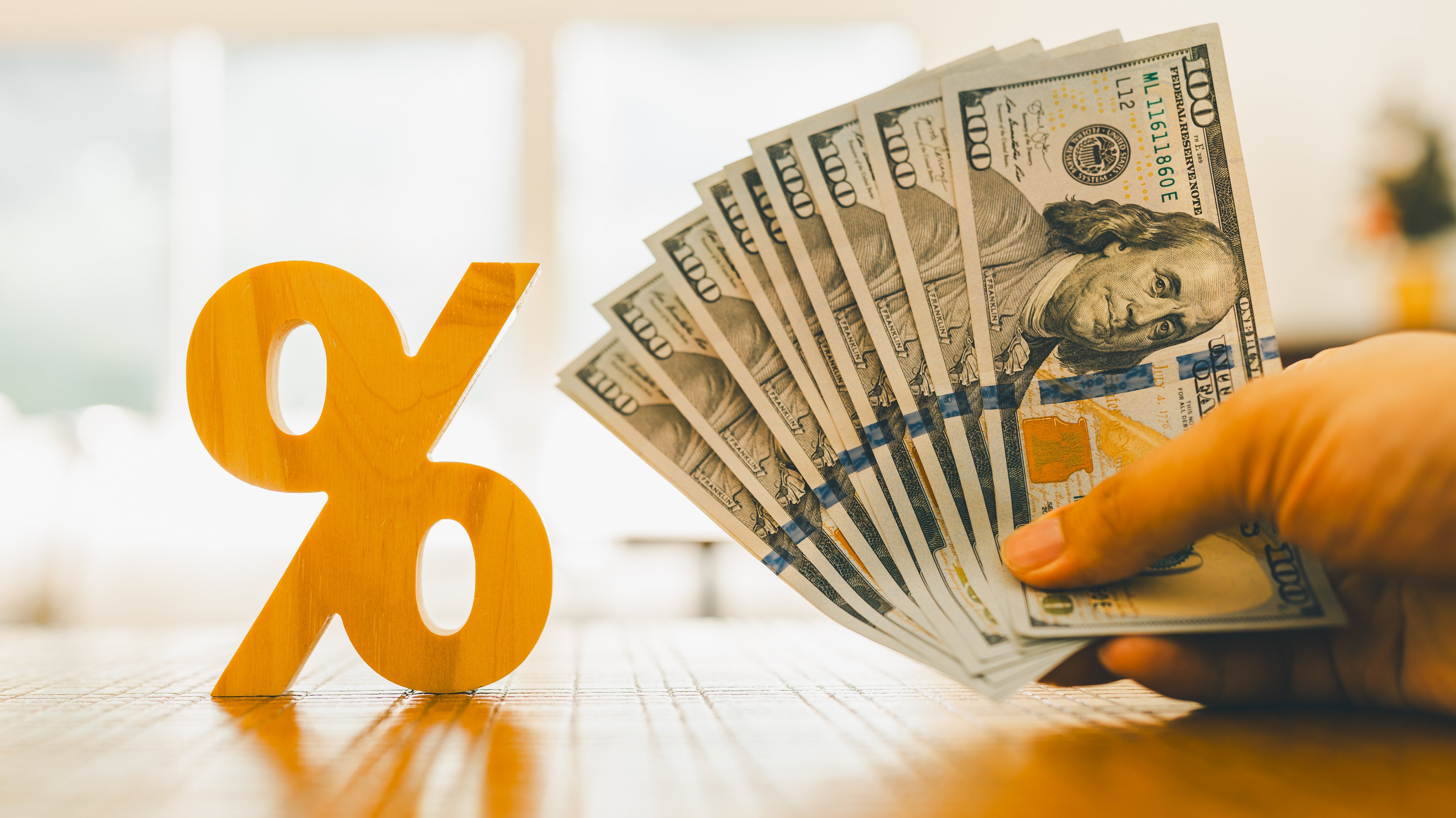 A handful of hundred-dollar bills shown next to a percentage sign.