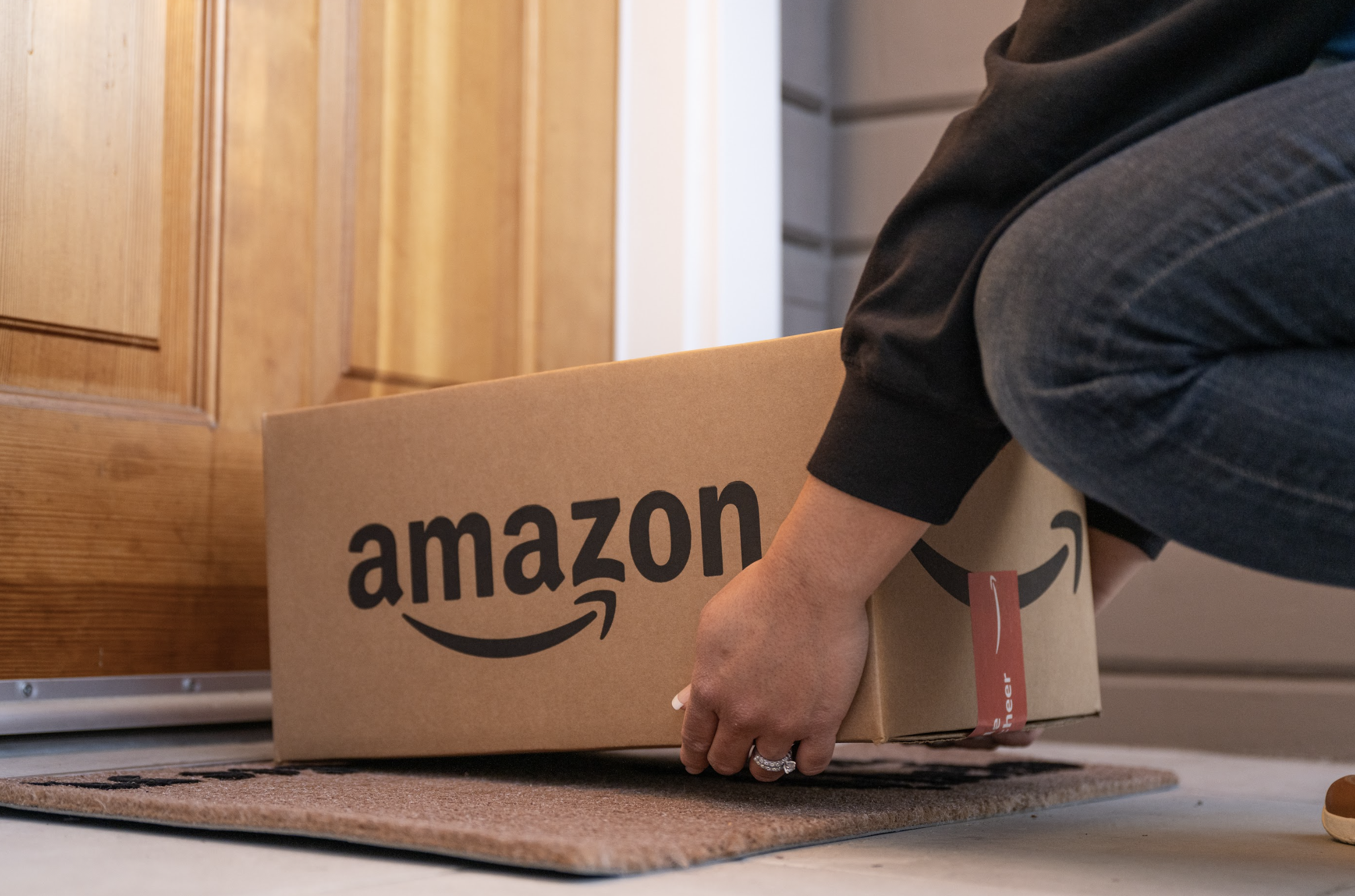 A person is lifting a cardboard box with an Amazon logo on it.