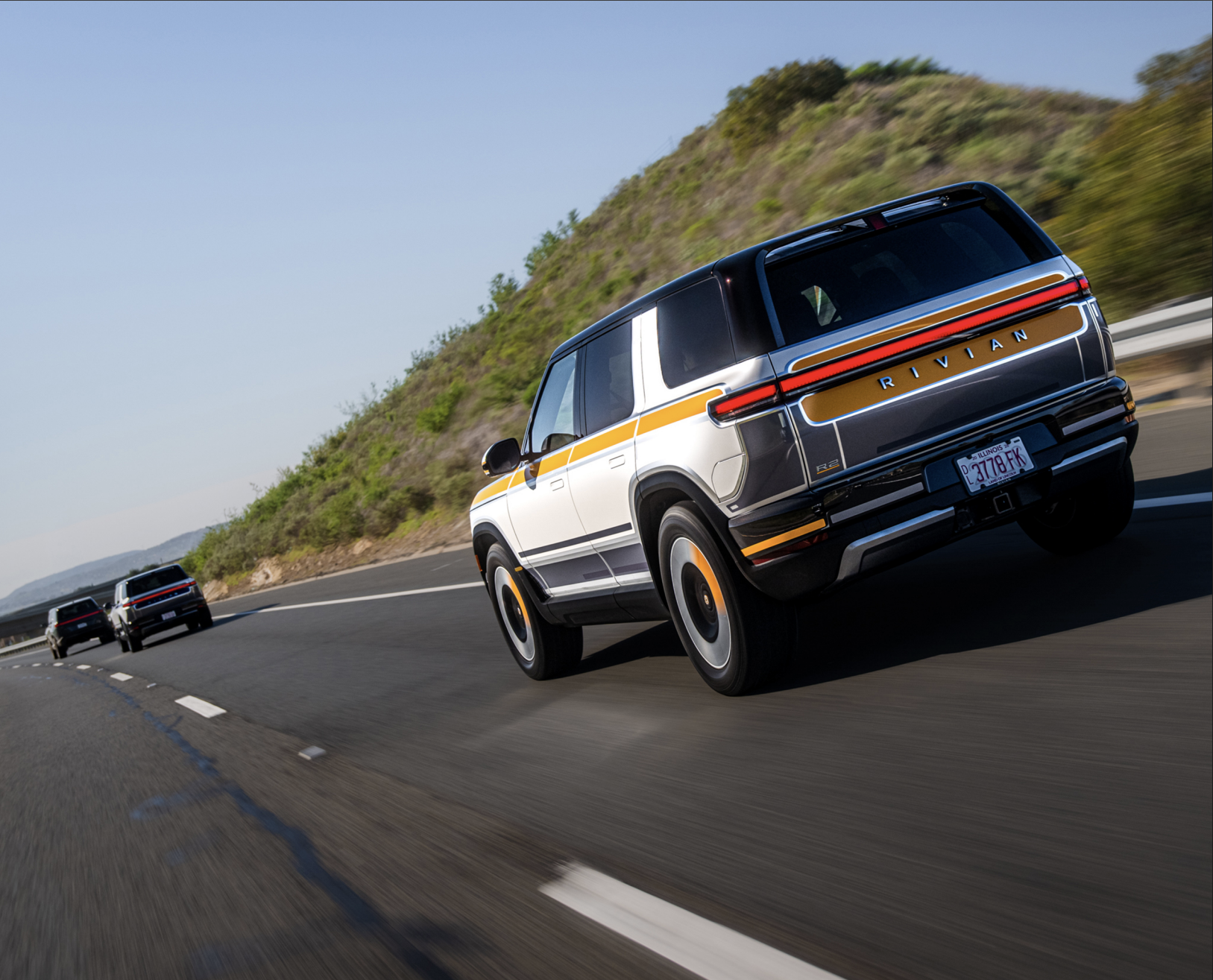 Three Rivian R2 SUVs with fancy paint job driving down highway.