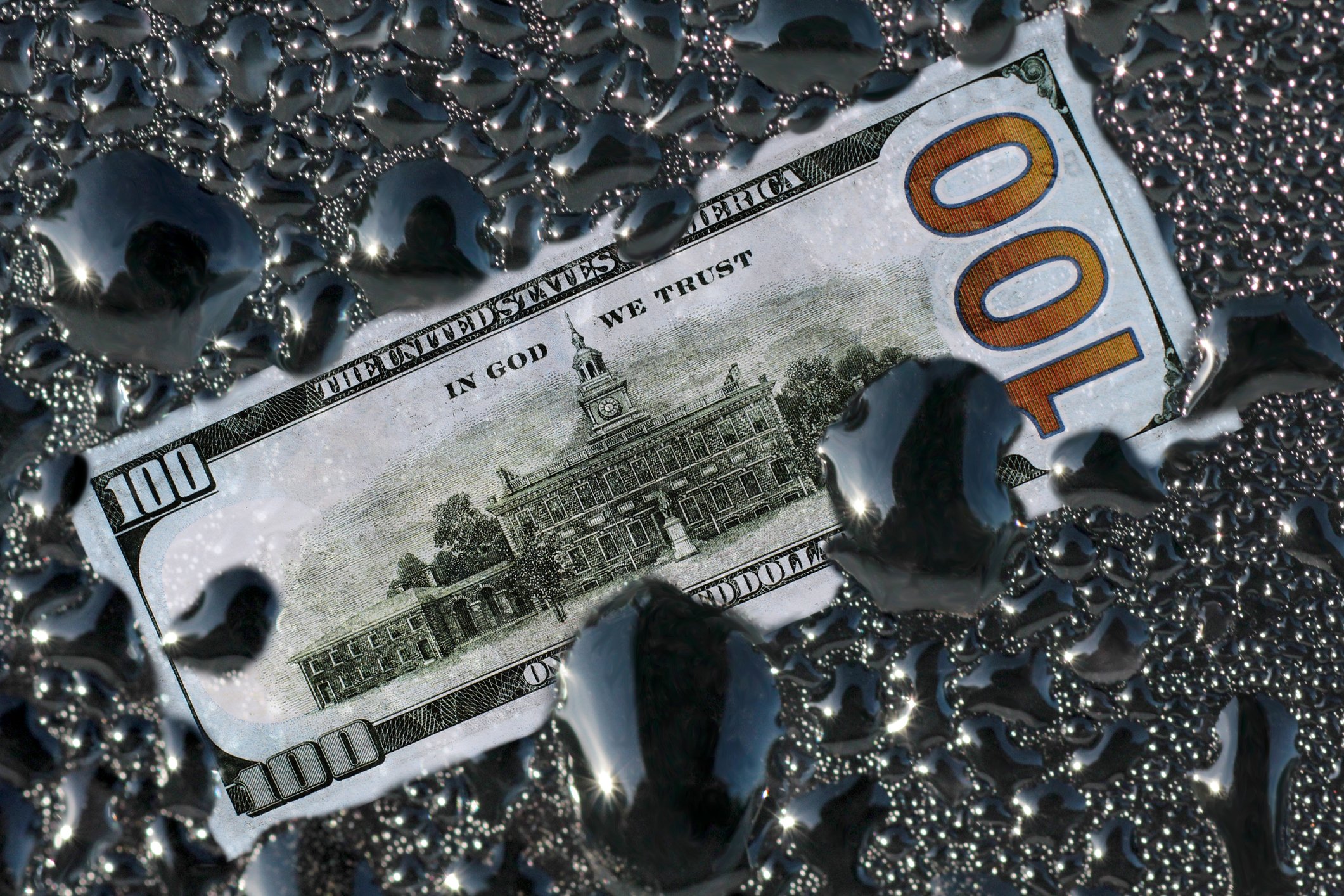 A $100 bill surrounded by drops of oil.