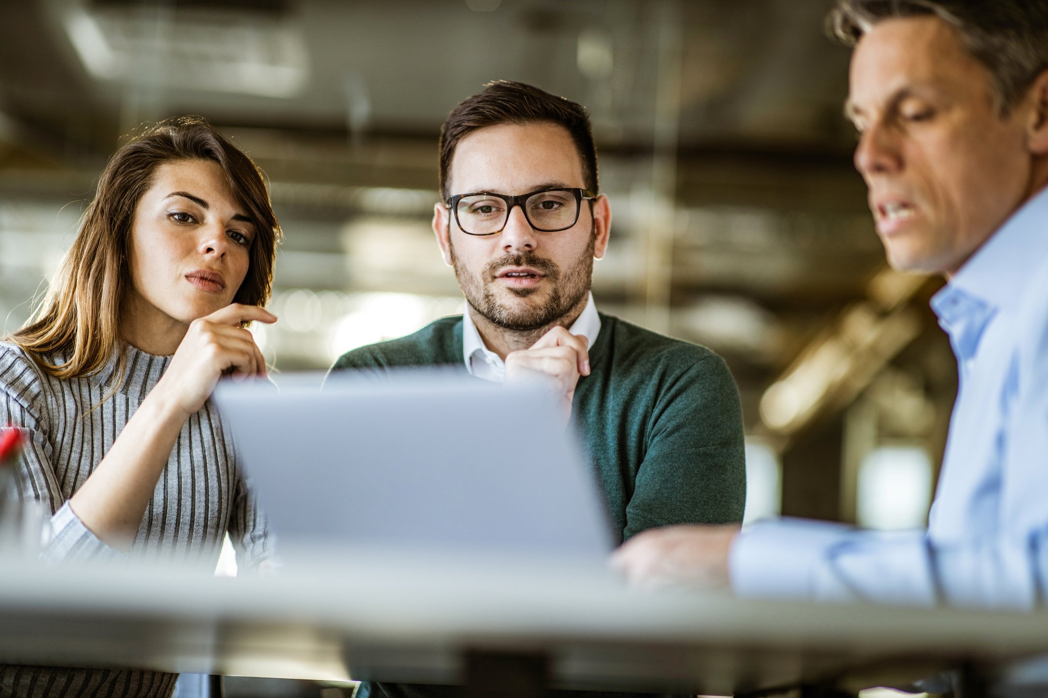 Three investors seated around a laptop discuss some data.