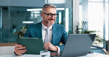 smiling businessman works on laptop and tablet.