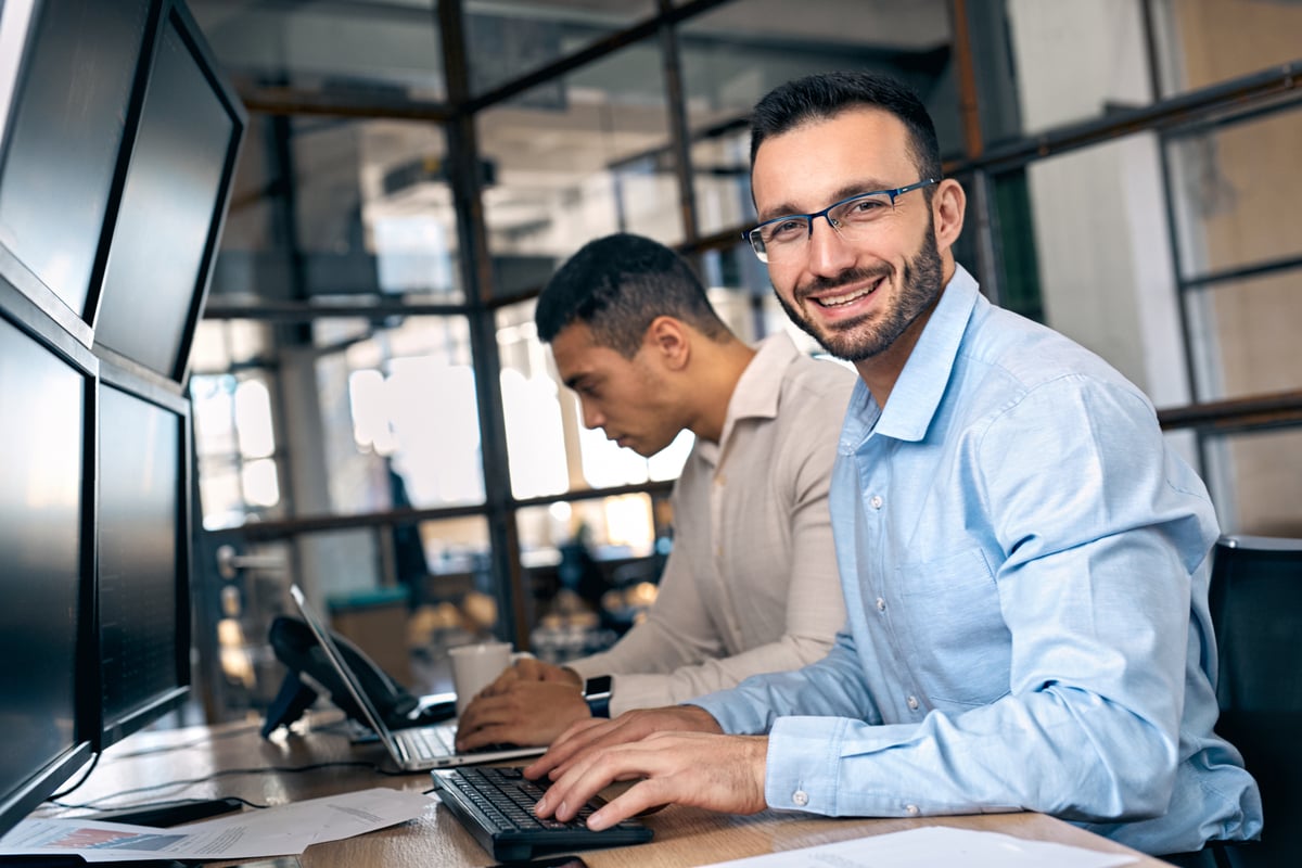 People working at a desk with many screens
