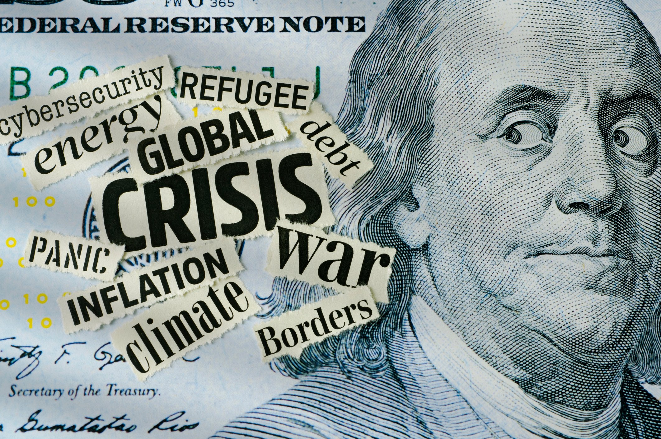 A $100 bill with Benjamin Franklin's eyes looking sideways at a group of newspaper clippings of words like Crisis, Debt, and Inflation.