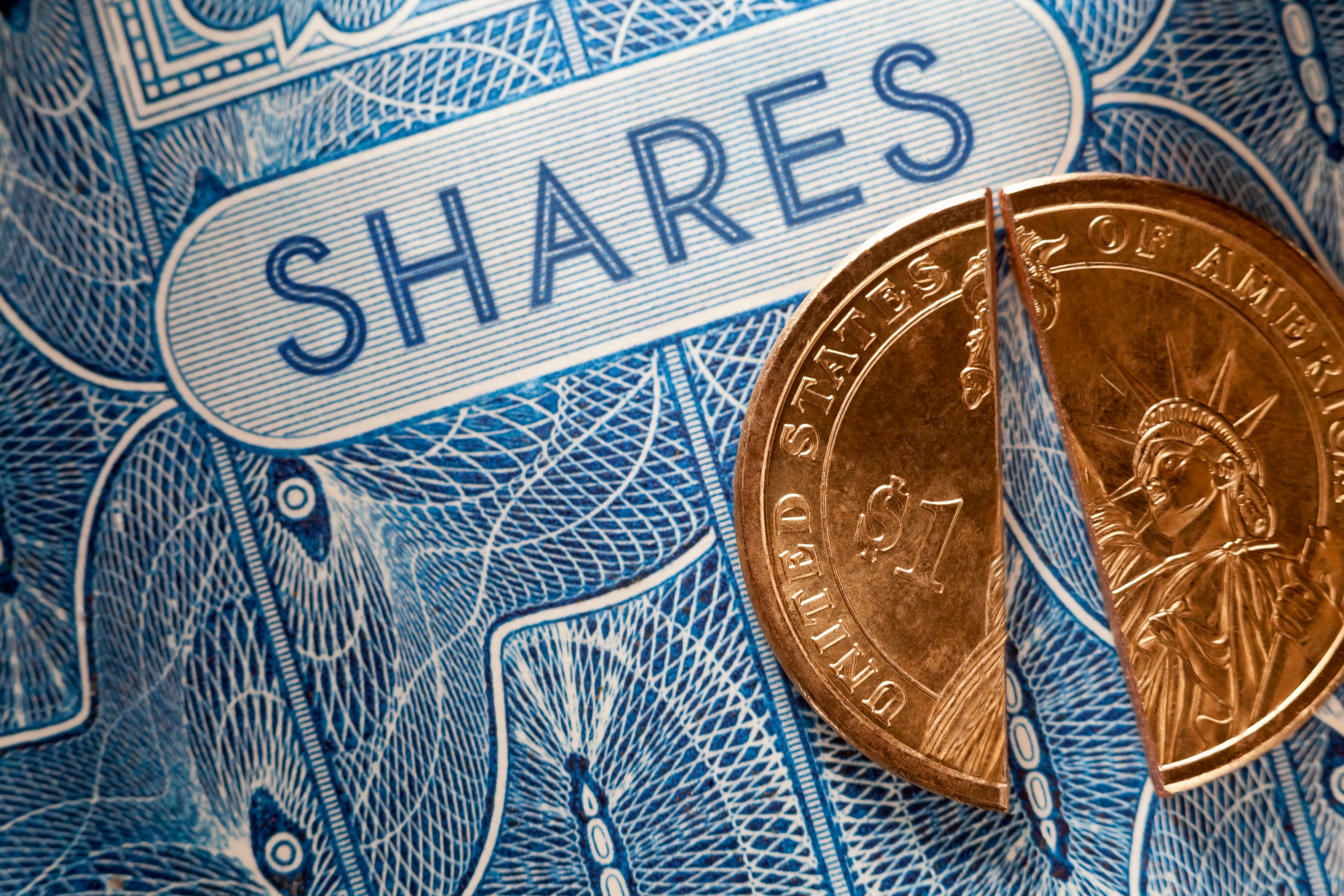 A gold coin split in half and placed on top of a blue stock certificate with the word "SHARES."