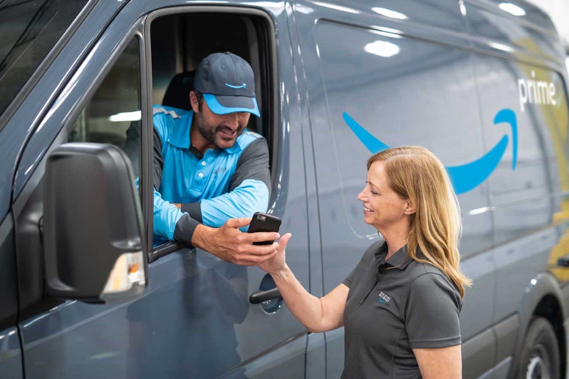 An Amazon delivery driver leaning out the window of their vehicle while speaking with a fellow employee.