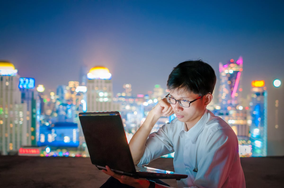 A worried investor looks at a laptop screen with a big city skyline in the background