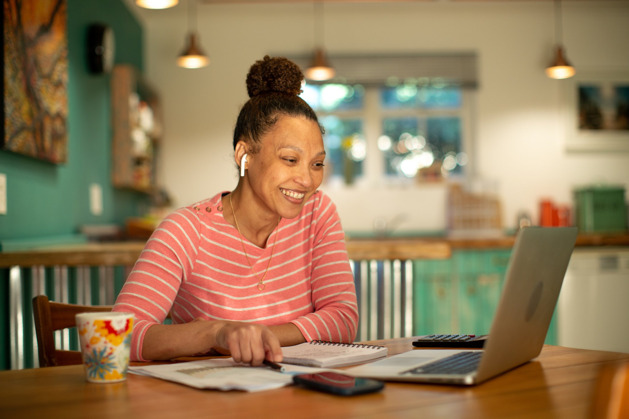 Smiling woman looking at laptop at kitchen table.