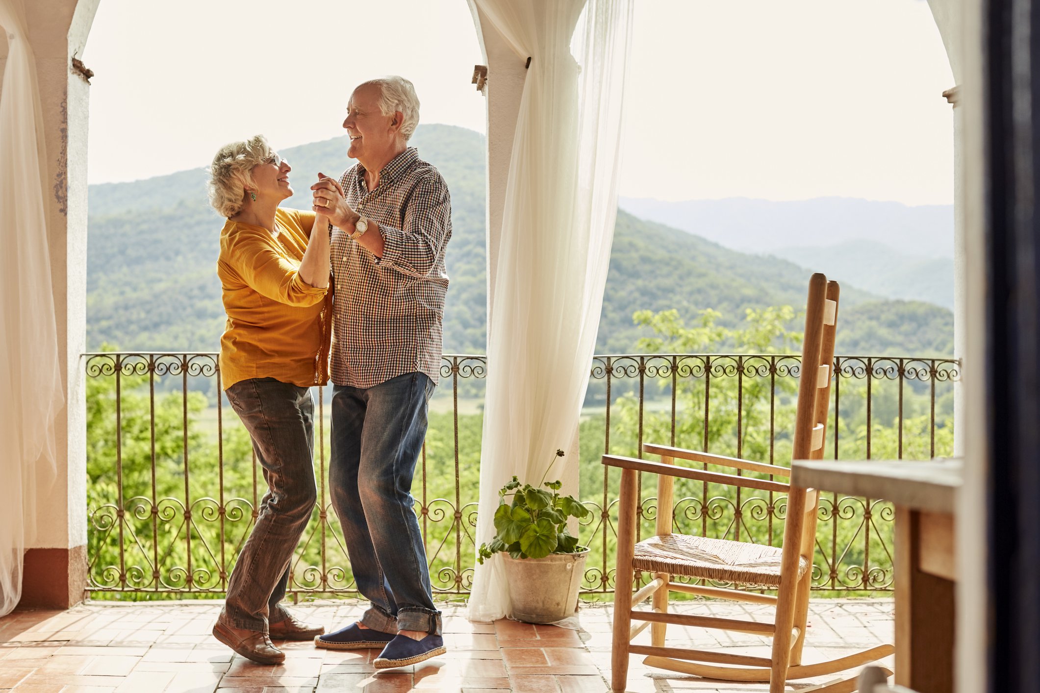 Senior couple dancing on patio overlooking mountainside.