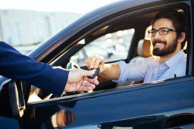 Person hands car keys to person sitting inside a car.