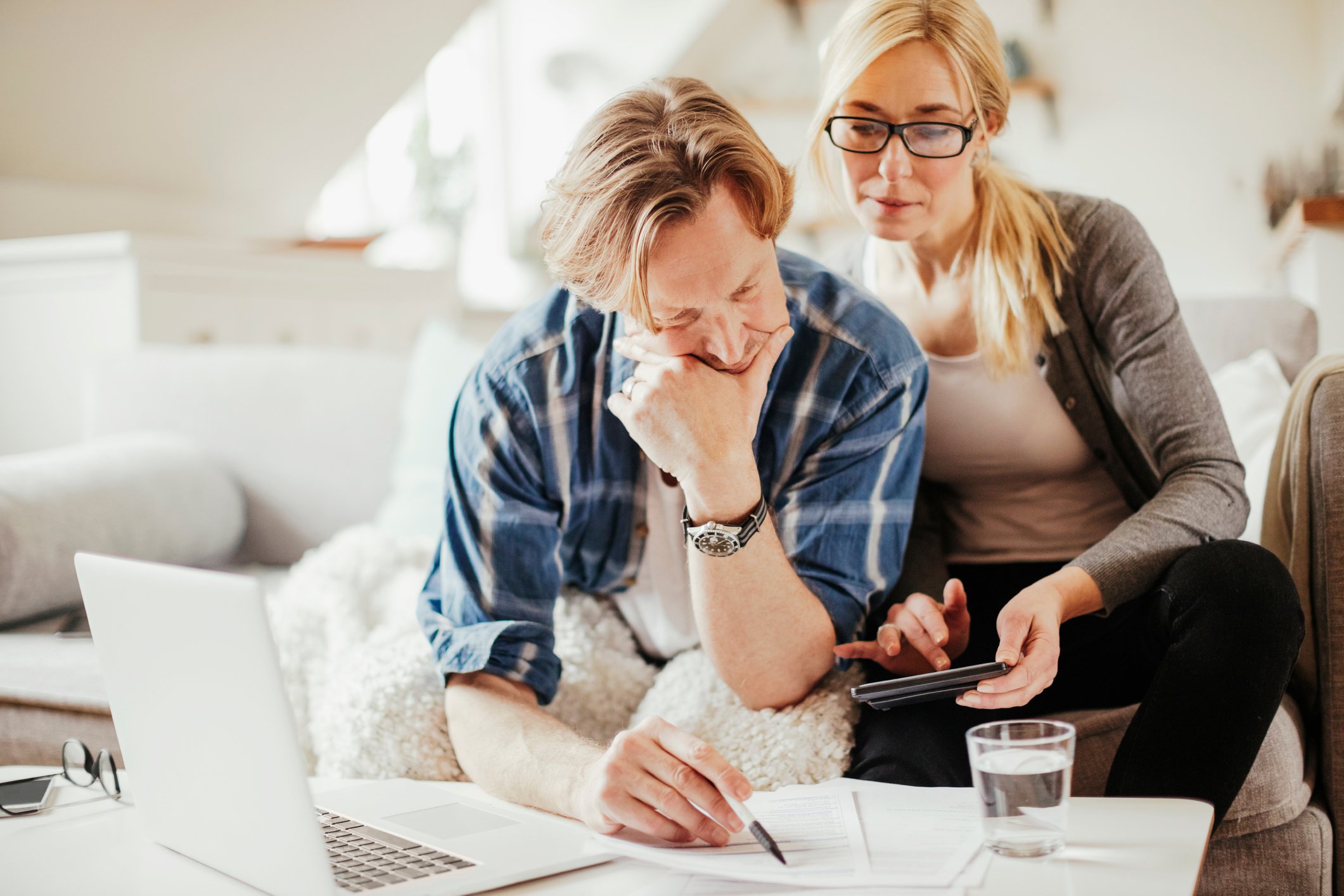 Couple using calculator and laptop while sitting on couch at home.