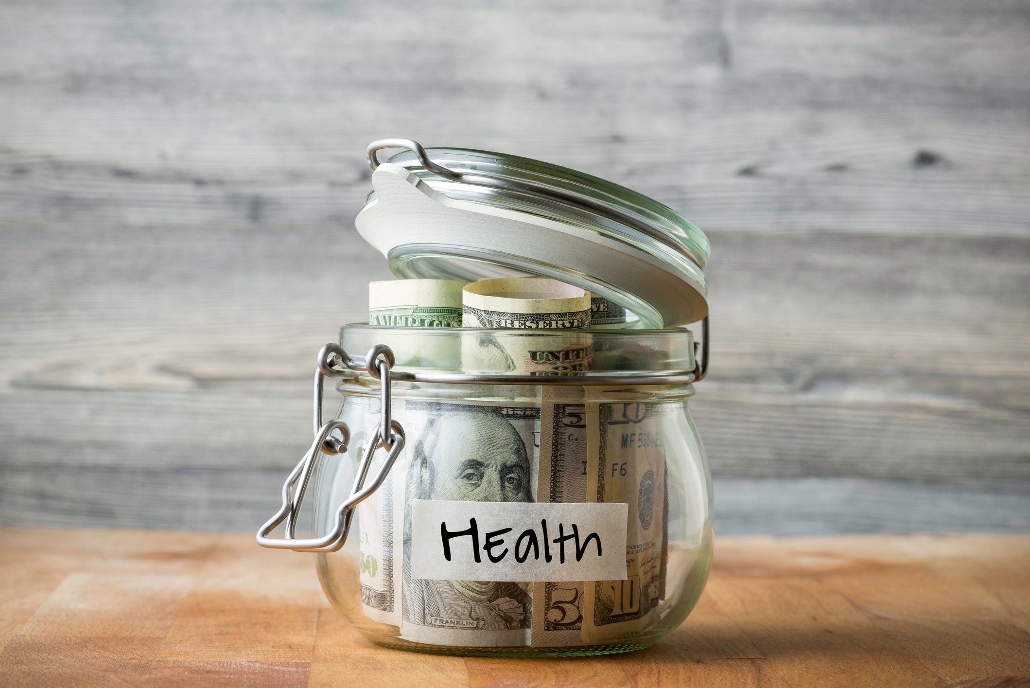 A glass money jar labeled health that's full of cash.