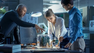 Three people leaning over and working on a model that sits on a desk in a technology lab.