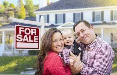 Smiling family in front of house with For Sale sign