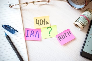 Sticky notes with 401k, IRA, Roth and a question mark on a desktop