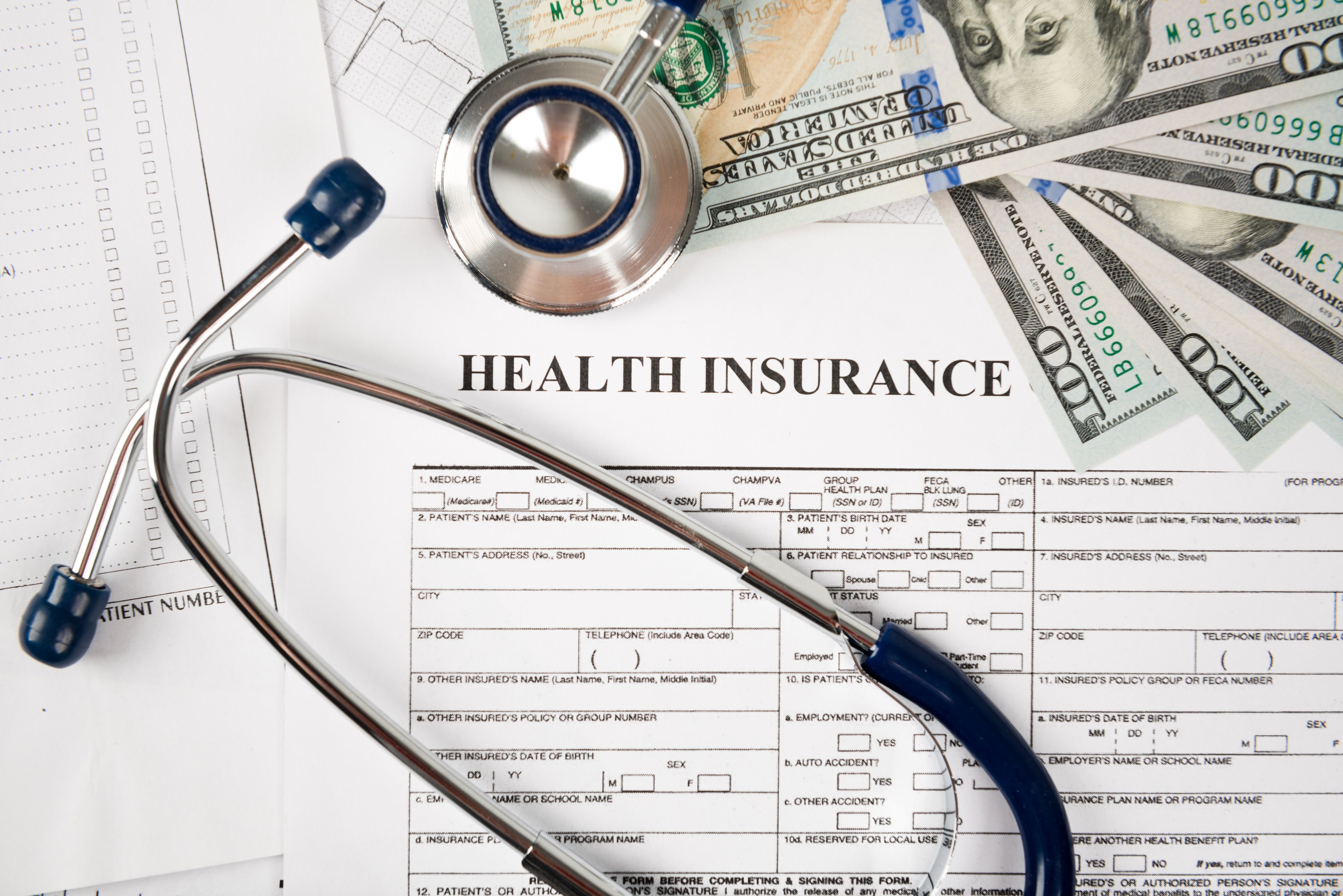 Health insurance paperwork with stethoscope and money on top