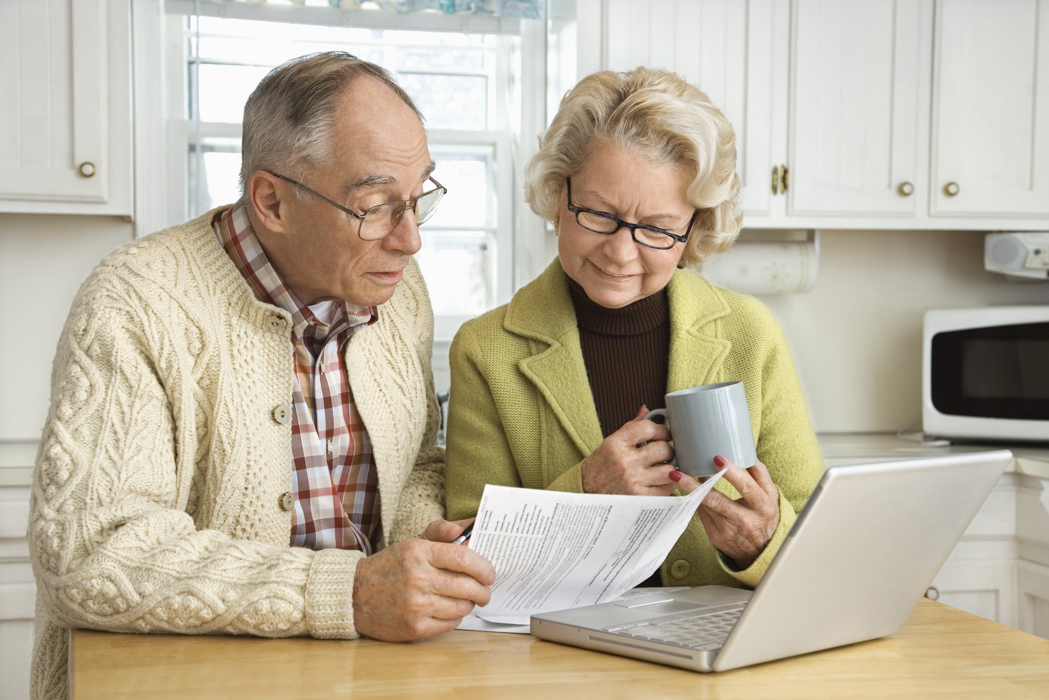 senior man and woman sitting at kitchen table and looking at papers in front of laptop