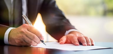Man in business suit signs his signature to paperwork